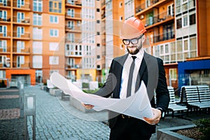Engineer in front of modern building with plan looking at blueprint