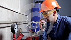 An engineer in glasses works in the boiler room, checks the maintenance of the heating system equipment