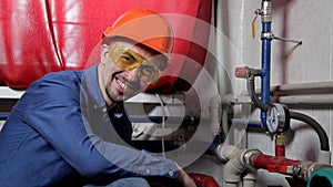 An engineer in glasses works in the boiler room, checks the maintenance of the heating system equipment