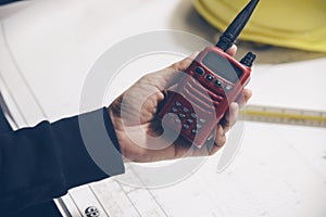 Engineer hand holding portable radio with drawings paper. Safety Officer inspector and checklist blueprint on construction site.