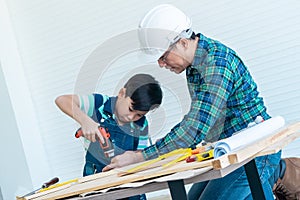 Engineer Handy Father is teaching his boy to use electric driller on wood