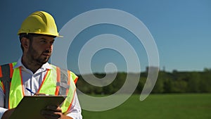 Engineer in a hard hat is writing notes while standing in the field