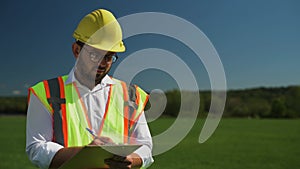 Engineer in a hard hat is writing notes while standing in the field. Construction of solar panels