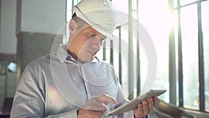 Engineer in hardhat is holding a tablet computer in a heavy industry factory. slow-motion