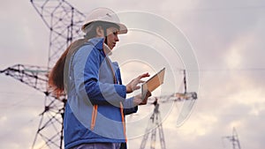 An engineer at a high voltage power plant works in a tablet at sunset in the sky, electrical energy design, industry