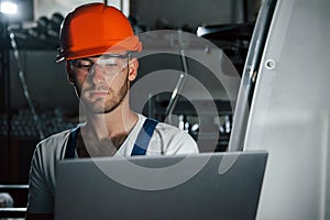 Engineer at his workplace with laptop. Man in uniform works on the production. Industrial modern technology