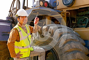 The engineer hold walky talky stand near the tractor and smile to show happy emotion of his work