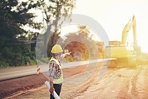 Engineer holding blueprint at road construction site with machinery