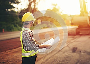 Engineer holding blueprint at road construction site with machinery background