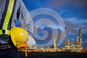 Engineer holding yellow helmet with oil refinery