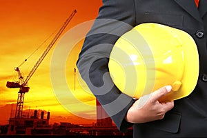 engineer holding yellow helmet for workers security on background of new highrise buildings and Silhouette Crane lifts