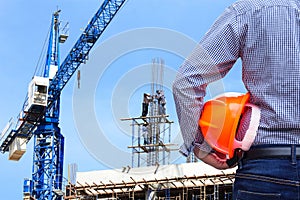 Engineer holding yellow safety helmet in building construction site with crane