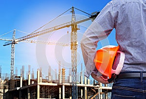 Engineer holding yellow safety helmet in building construction site with crane