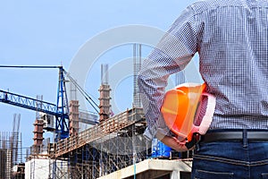 Engineer holding yellow safety helmet in building construction site with crane