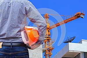 Engineer holding yellow safety helmet in building construction site with yellow crane