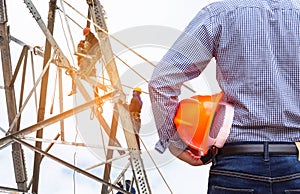 Engineer holding yellow safety helmet with electricians working on pylon construction tower