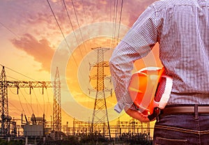 Engineer holding yellow safety helmet with high voltage electric pylon substation on sunset