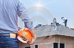 Engineer holding yellow safety helmet at new home building with workers installing concrete tile