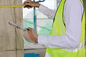 Engineer or home inspector in green reflective jacket checking review document and inspecting with clipboard at construction site