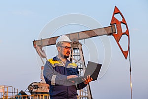 Engineer with a laptop on the background of an oil pump