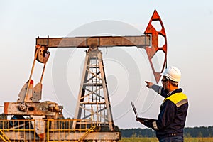 Engineer with a laptop on the background of an oil pump
