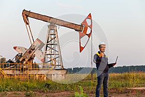 Engineer with a laptop on the background of an oil pump