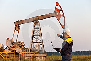 Engineer with a laptop on the background of an oil pump