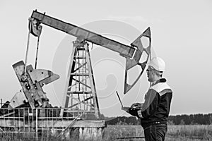 Engineer with a laptop on the background of an oil pump. Black and white photography