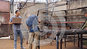 An engineer with a laptop in a workshop for the production of metal products walks around the workshop among workers