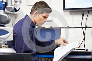 Engineer Looking At Plans With CMM Arm In Foreground