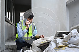 Engineer male manager wearing yellow vest talking on mobile phone under new building