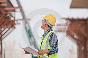 Engineer man with blueprint checking project at construction site, Foreman worker holding plan in building site