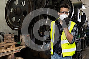Engineer man wearing face mask and and using walkie-talkie while reporting on machine process