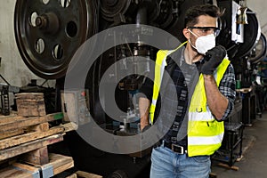 Engineer man wearing face mask and and using walkie-talkie while reporting on machine process