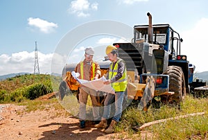 Engineer manager discuss with his team and stand in front of tractor in the area of construction