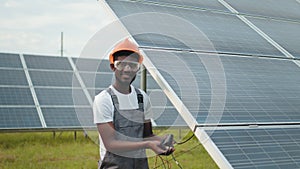 Engineer measuring amperage in solar panels outdoors. African man in grey overalls measuring resistance in solar panels