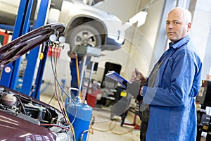 Engineer with notebook during car air conditioner refilling