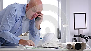 Engineer in office talking business t a cell phone looking to technical plans