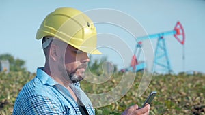 Engineer oilman works with a mobile phone. Oil drill, field pump jack. Oil field, the oil workers are working. The