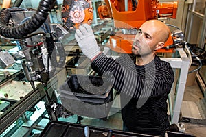 Engineer optimizing production by robotic arm in automotive smart factory, employee in industry, industrial concept