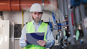 Engineer plumber with tablet records water meter readings in boiler room.