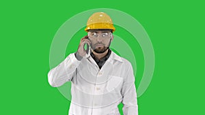 Engineer in protective glasses and hat walking, taking on the phone on a Green Screen, Chroma Key.