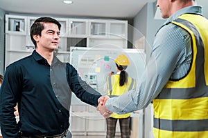 An engineer with a protective vest handshake with an investor in his office