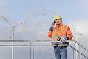 Engineer with protective work wear talking on mobile phone in front of wind turbines