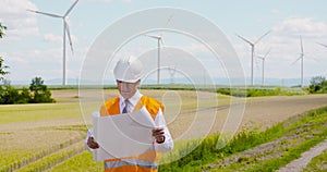 Engineer reading plan against wind turbine farm
