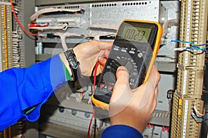 Engineer`s hands close-up with a multimeter test industrial cabinet of relay protection and automation