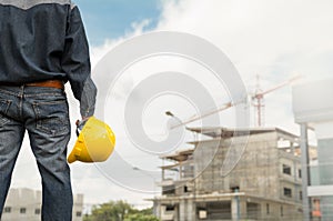 Engineer or safety officer holding yellow helmet with the building is background in construction site.