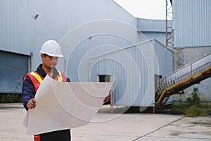 Engineer in safety uniform and white helmet holding project plan at construction outdoor site background