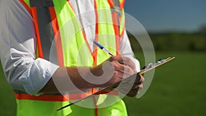 Engineer in a safety vest is writing notes while standing in the field. Technical maintenance