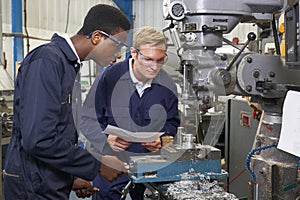 Engineer Showing Apprentice How to Use Drill In Factory